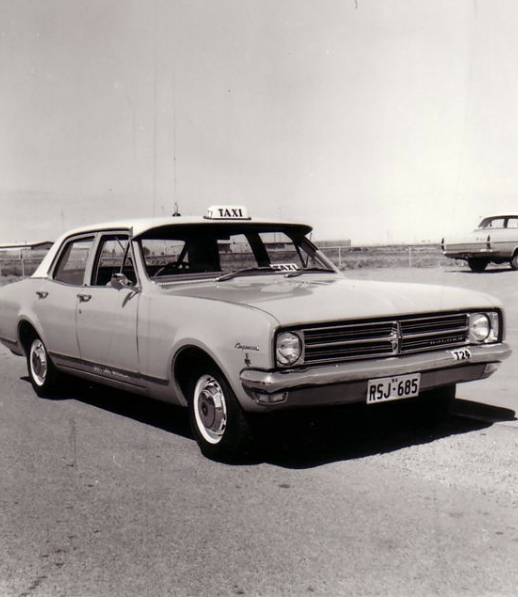 Black and white photo of an early Des's taxi sedan with roof sign